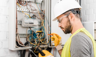 Electrician checking electrical box with multimetr in corridor