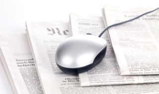 Computer mouse laying on top of a paper newspaper stack