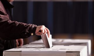 Hand of a person casting a vote into the ballot box during elections