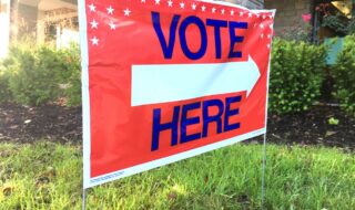 Large Orange background colored placard with Bold blue lettering that says Vote here