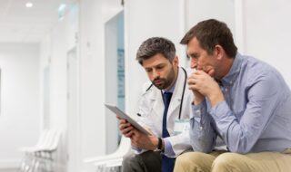 A Doctor and a patient sitting down at a hospotail and looking over some medical charts at the office.