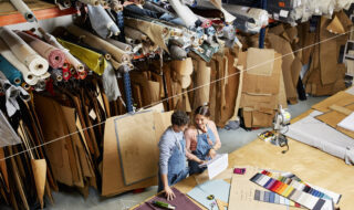 Workers Discussing Over Book At Workbench In Sofa Workshop